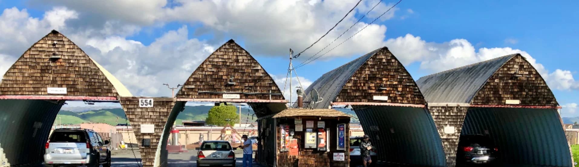 The original Milpitas coin wash: four shingled A-framed manual bays with cars parked inside, the number 554 painted on the second arch